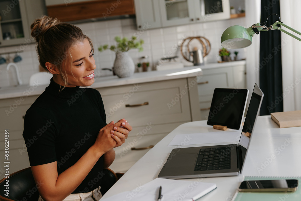 Beautiful young female entrepreneur looking at laptop while having video call at the home office Beautiful young female entrepreneur looking at laptop while having video call at the home office