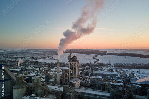 Aerial view of cement plant production area with high concrete factory structure and tower cranes at industrial site. Greenhouse gas smoke polluting air. Manufacture and global industry concept