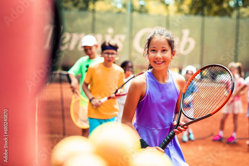 Young girl with a smile holding a tennis racket among other junior players photo