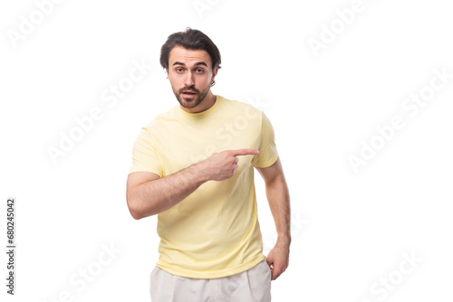 young brutal brunette man in a T-shirt points his hand to the side on a white background with copy space