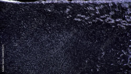 Clear drinkable natural mineral water pouring into a glass. Extreme macro close-up of carbonated H2O filling full screen on clean black background. Refreshing stream of rising pure clean bubbly liquid
