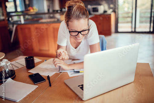 Smiling young woman in casual clothing using laptop working from home