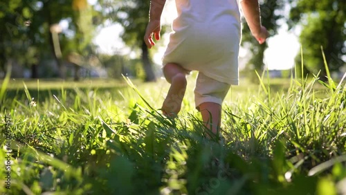 Boy kid run on grass in summer in park. Feet close up on green grass in sun. Kid dream in nature. Children play in the park on vacation. Active child jogging on a picnic in summer in a park in nature photo