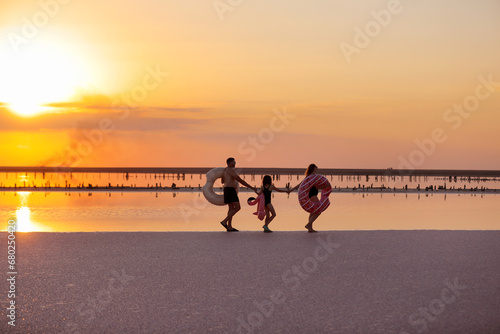 happy family walk on sunset by the sea. mom, dad and child daughter having fun on summer holiday vacation in nature. travel kid dream concept. dramatic sunset