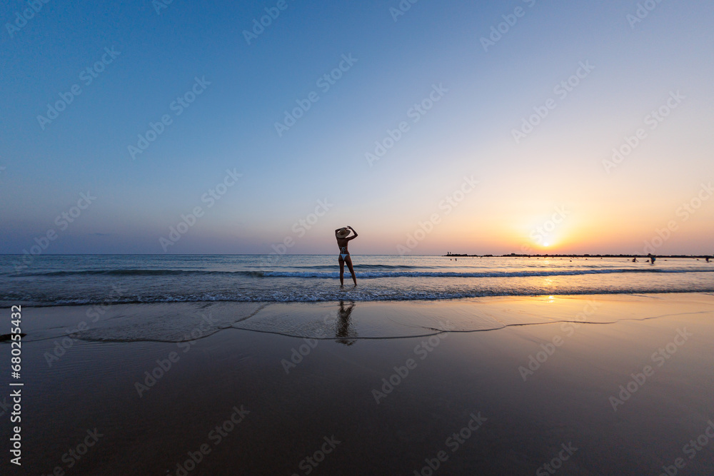 silhouette of a woman walking along the seashore. Spiritual Peace Meditation. A happy girl walks along the seashore against the backdrop of sunset.