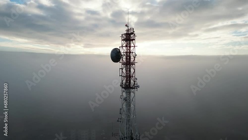 tall communications tower high in the sky and the clouds, dense fog around on a beautiful sunny morning, camera on drone circling around the tower showing the antennas and aerials