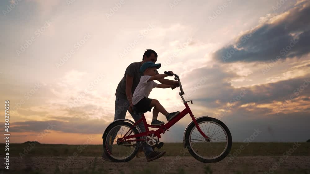 Father's Day. Father teaches his son to ride bike. Kid son learn to ride bike at sunset in park. Happy family on bike in summer meadow. Active game with bicycle at picnic father and son play in summer Father's Day. Father teaches his son to ride bike. Kid son learn to ride bike at sunset in park. Happy family on bike in summer meadow. Active game with bicycle at picnic father and son play in summer