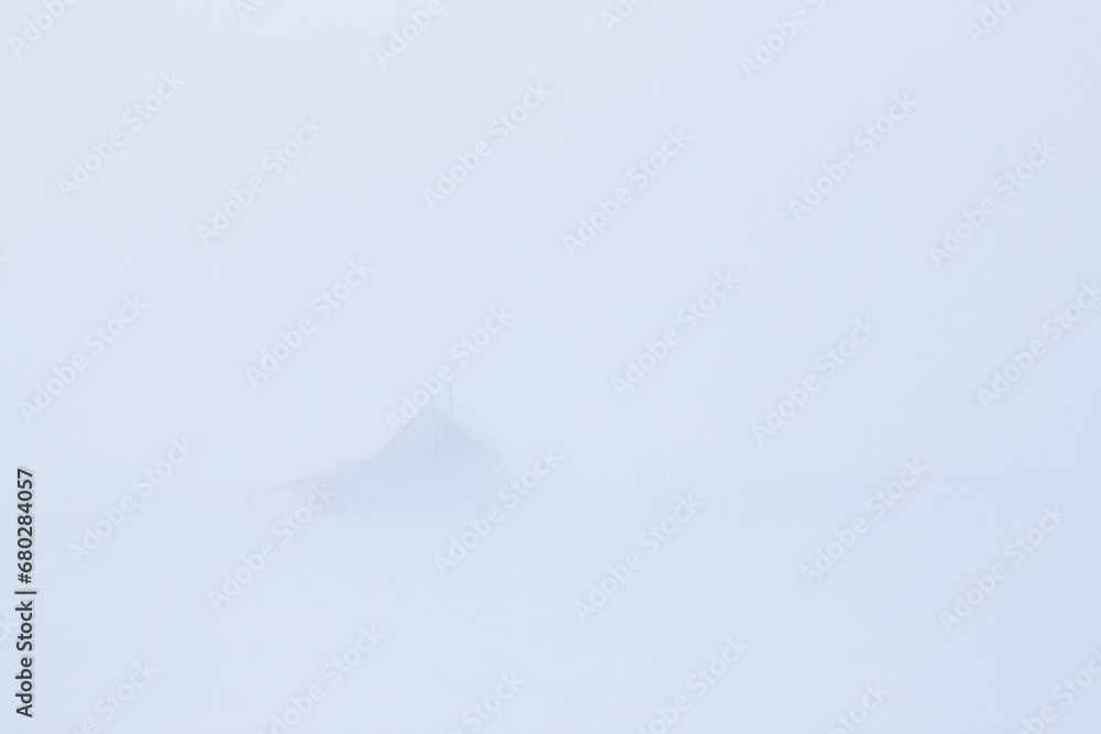 Winter arctic landscape. View of a house in a snowy tundra. Poor visibility during a blizzard and snow storm. Abandoned building in the Arctic. Chukotka, Siberia, Far North Russia. Blurred background.