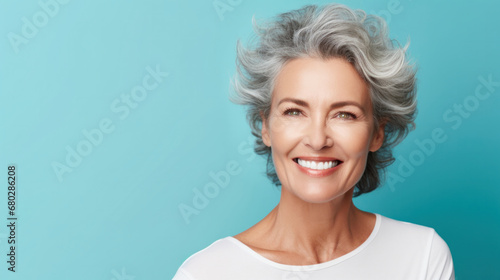 Radiant senior woman with silver hair, bright smile, on a turquoise background, embodying vitality and joy