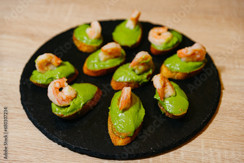 Bruschetta with avocado puree and shrimp on a black slate board, appetizer presentation