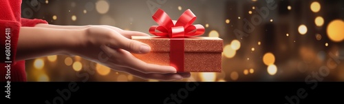 Christmas, birthday or valentine's day celebration, a person holding a beautiful gift bow with ribbon and bow on blurred dark background with lights and bokeh, magic festive emotion and atmosphere