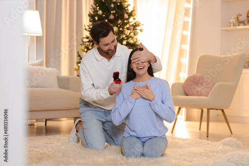 Making proposal. Man with engagement ring surprising his girlfriend at home on Christmas photo