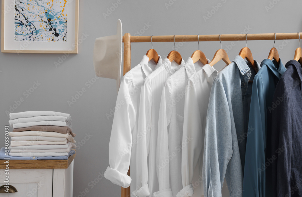 Rack with different stylish shirts, hat and chest of drawers near grey wall in room. Organizing clothes Rack with different stylish shirts, hat and chest of drawers near grey wall in room. Organizing clothes
