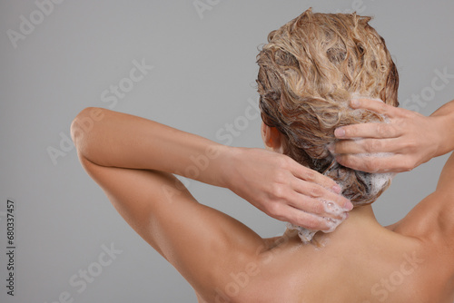 Woman washing hair on light grey background, back view. Space for text