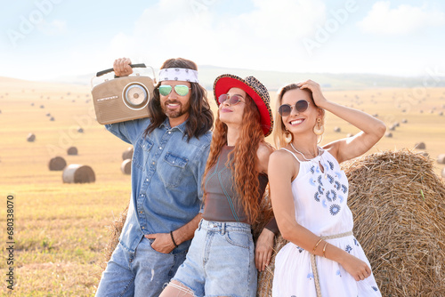 Happy hippie friends with radio receiver near hay bale in field
