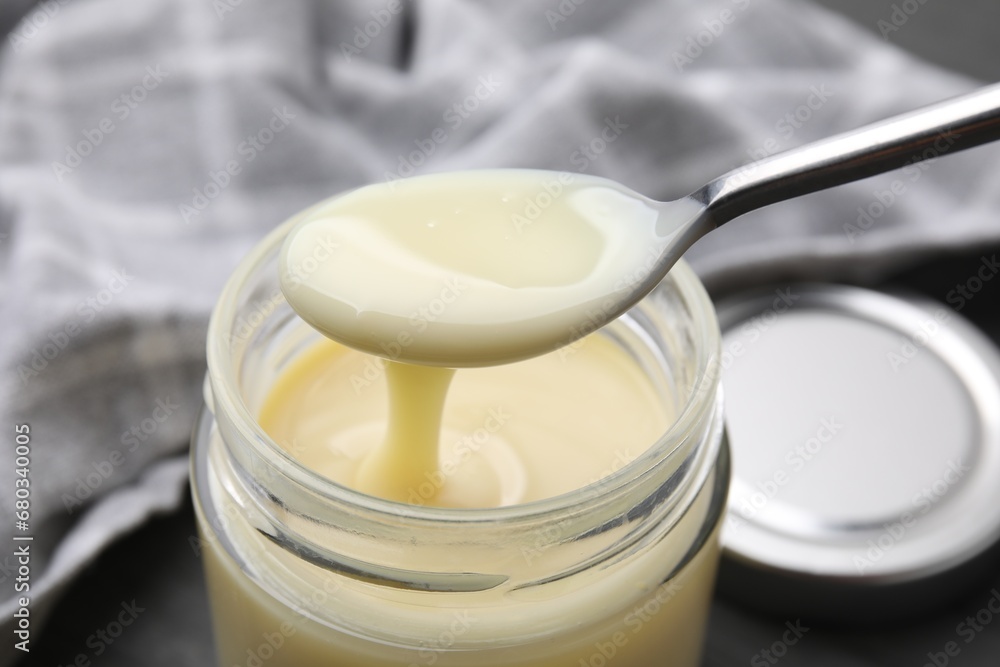 Condensed milk flowing down from spoon into jar on table, closeup Condensed milk flowing down from spoon into jar on table, closeup