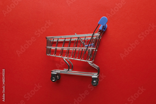 Small metal shopping cart on red background, top view