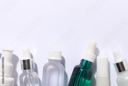 Many bottles of cosmetic serum on white background, flat lay. Space for text
