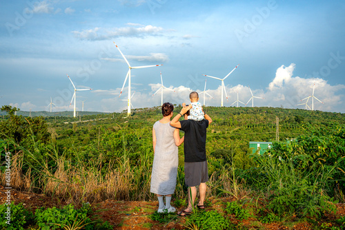 A happy young family looks at wind turbines. Wind turbines are alternative sources of electricity, the concept of sustainable resources and renewable ener © Quang