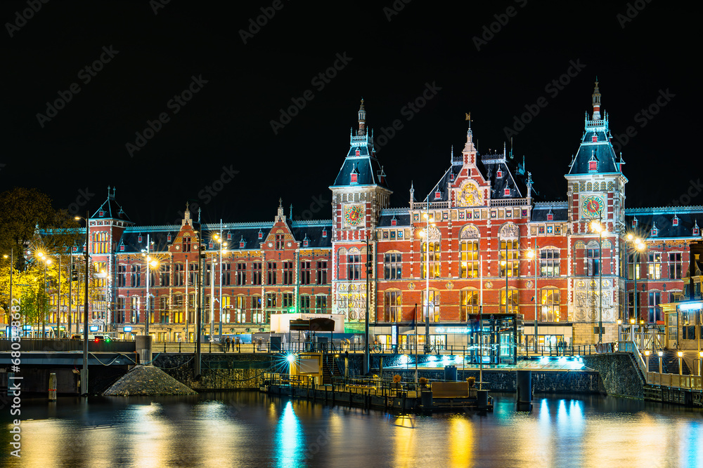 Fototapeta premium Długa ekspozycja nocnego zdjęcia Dworca Centralnego w Amsterdamie. Zachwycające oświetlenie na tle ciemnego nieba, uwydatniające piękno charakterystycznej architektury.