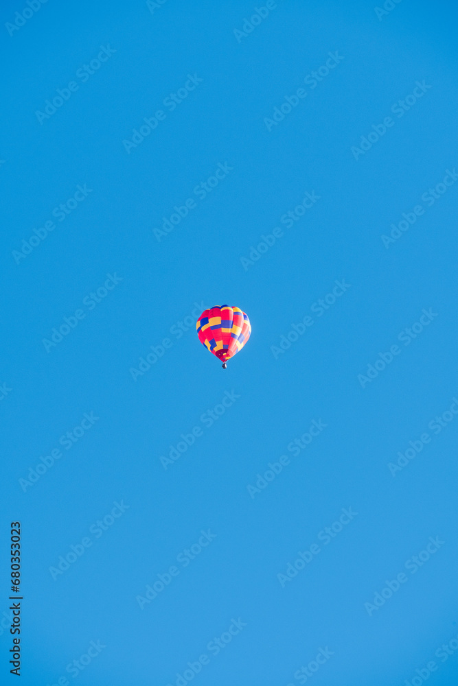 A solitary red, yellow, and blue hot air balloon in flight, surrounded on all sides by empty space with a pure blue sky. A solitary red, yellow, and blue hot air balloon in flight, surrounded on all sides by empty space with a pure blue sky.