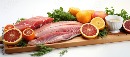 On a white table isolated in a white background, a variety of food items can be seen including white fish, orange slices, lemon zest, and cooking meat, creating a beautiful display for a healthy