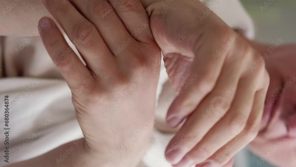 Vertical video. Painful joints. Elder man. Age changes. Unrecognizable senior male massaging hands becoming numb sitting sofa light home room interior.