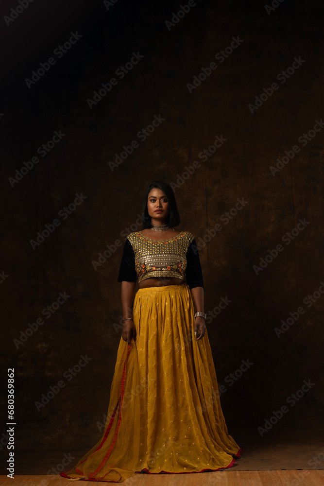 girl wearing indian wear - black blouse and yellow lehenga and dupatta beautiful makeup holding flowers in her hand in black background