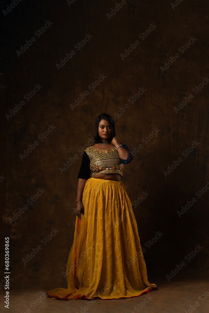 girl wearing indian wear - black blouse and yellow lehenga and dupatta beautiful makeup holding flowers in her hand in black background