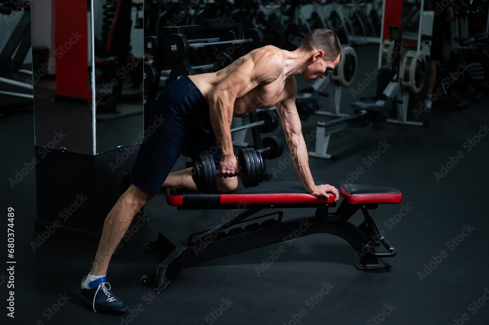 Shirtless man doing dumbbell row to waist on bench at gym. Shirtless man doing dumbbell row to waist on bench at gym.