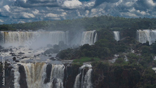 Beautiful cascades of waterfalls. Streams of water falling from the ledges are shrouded in spray, fog. Green vegetation, rocks in the riverbed. Clouds in the sky. Iguazu Falls. Brazil © Вера 
