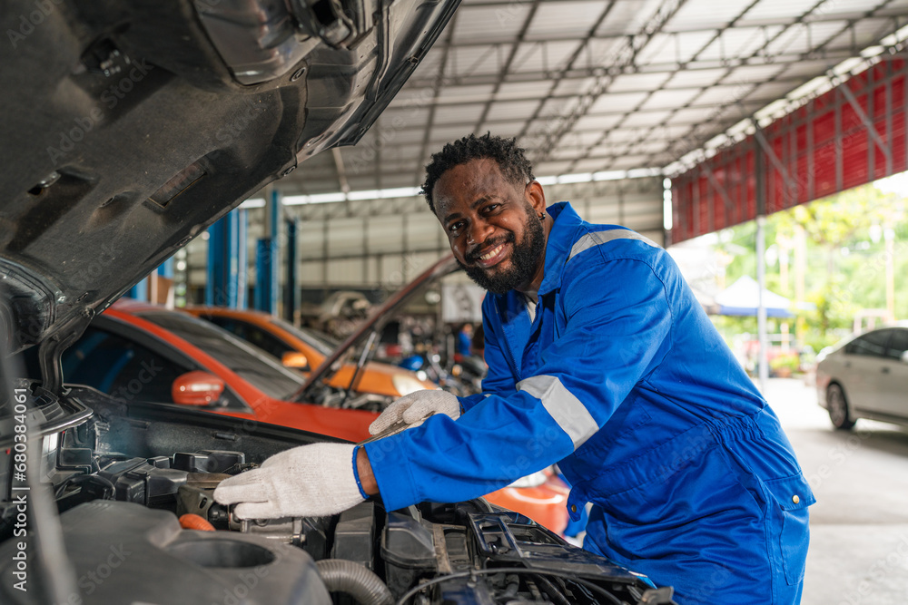 Mechanic working under the hood at the repair garage. Portrait of a happy mechanic man working on a car in an auto repair shop. Male mechanic working on car. Mechanic working under the hood at the repair garage. Portrait of a happy mechanic man working on a car in an auto repair shop. Male mechanic working on car.