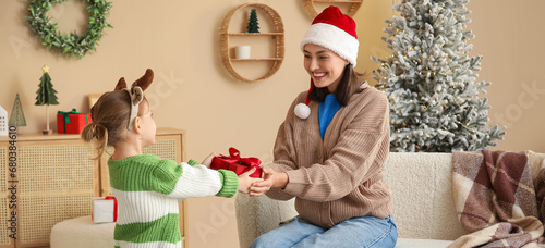 Cute little girl giving her mother Christmas gift at home