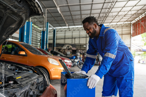 Mechanic working under the hood at the repair garage. Portrait of a happy mechanic man working on a car in an auto repair shop. Male mechanic working on car.