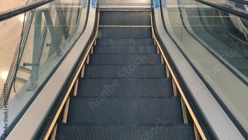 Close up of an escalator going down. The steps of the escalator are made of metal, and they are coated in a rubber material. Located in a public place, such as a mall or train station