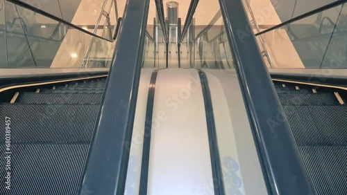 Couple of escalators going up and down. The escalators are located in a public space, such as a shopping mall or airport. The escalators are flanked by two walls, one on the left and one on the right