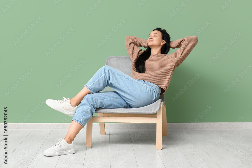 Beautiful young woman resting in comfortable chair near green wall Beautiful young woman resting in comfortable chair near green wall