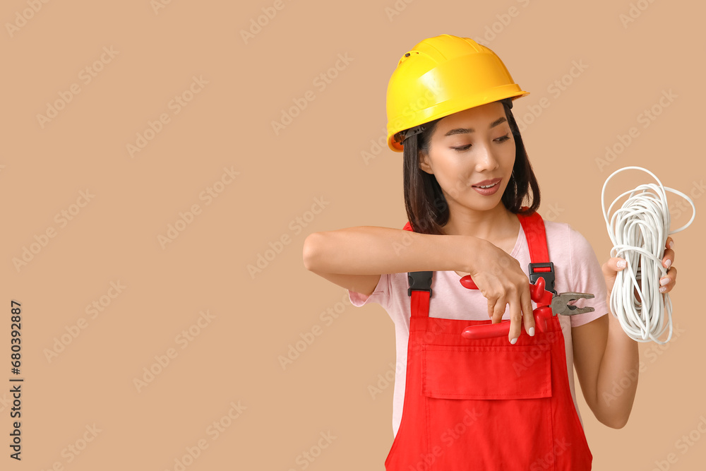 Young female electrician with pliers and cables on beige background Young female electrician with pliers and cables on beige background