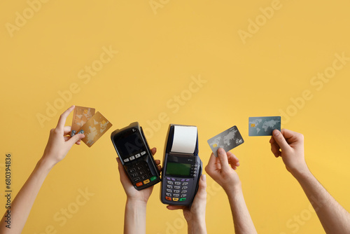 Female hands with payment terminal and credit cards on yellow background photo
