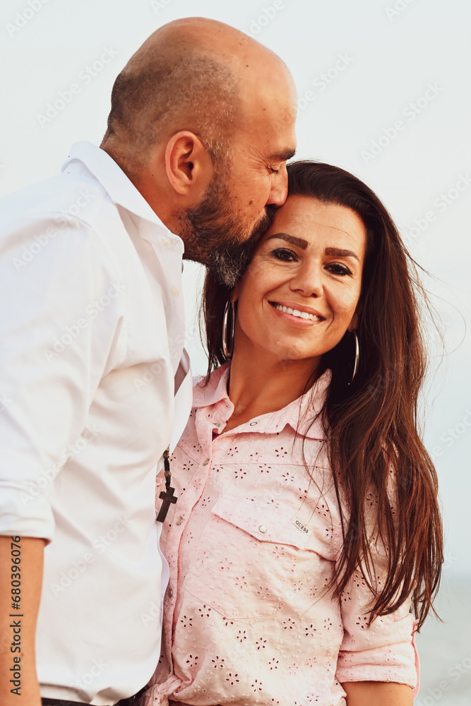 Happy smiling Couple drinking vine at Sand Dunes near the Beach. Young happy Bearded muscular man in White shirt kissing and hugging beautiful woman at sunset on a beach Happy smiling Couple drinking vine at Sand Dunes near the Beach. Young happy Bearded muscular man in White shirt kissing and hugging beautiful woman at sunset on a beach