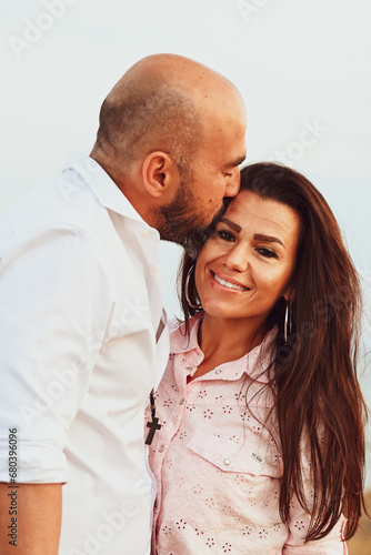 Happy smiling  Couple drinking vine at Sand Dunes near the Beach.  Young happy Bearded muscular  man  in White shirt kissing and hugging beautiful woman at sunset on a beach