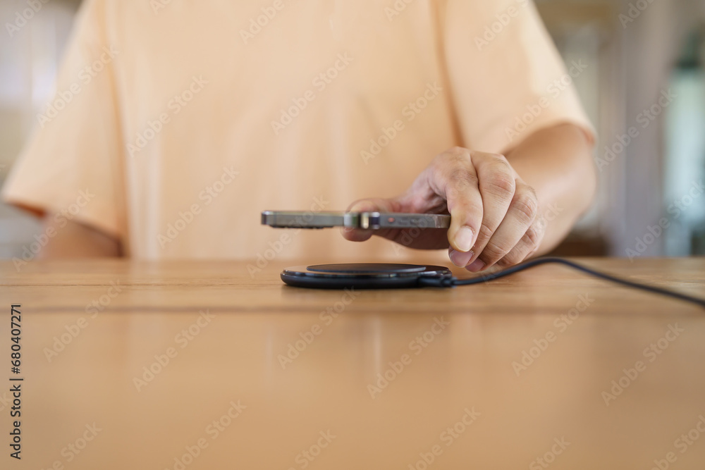 Fototapeta premium Charging mobile phone battery with wireless charging device in the table. Smartphone charging on a charging pad. Mobile phone near wireless charger Modern lifestyle technology concept.