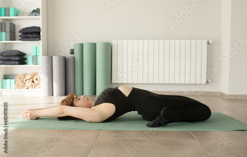 Young attractive smiling woman practicing yoga, wearing sportswear, pants and top, indoor full length at home. Sport, fitness, health care and lifestyle. 