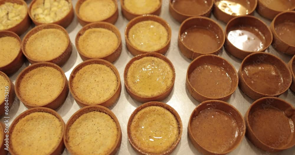 A large number of mini-tarts are laid out in even rows on a professional pastry table in the process of impregnating them with apple syrup with the help of a pastry brush. A large number of mini-tarts are laid out in even rows on a professional pastry table in the process of impregnating them with apple syrup with the help of a pastry brush.