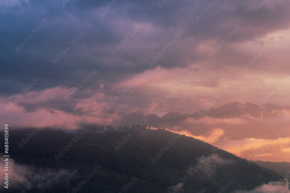 Fog and clouds in the mountains against the backdrop of the setting sun, changeable weather in the mountains, clouds and nebula on mountain peaks