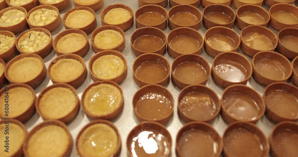 A large number of mini-tarts are laid out in even rows on a professional pastry table in the process of impregnating them with apple syrup with the help of a pastry brush. A large number of mini-tarts are laid out in even rows on a professional pastry table in the process of impregnating them with apple syrup with the help of a pastry brush.