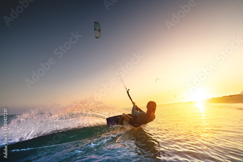 girl kiter rides against a beautiful background of splashes and a colorful sunset of the sea. Woman kitesurfing on the water with a fantastic view in the background photo