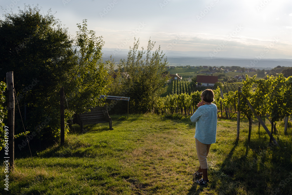 A woman in a vineyard looks at the surroundings at sunset