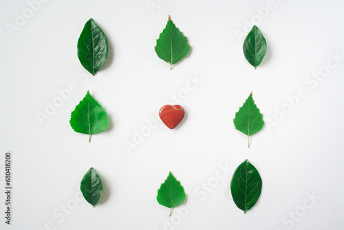 Red heart stone toy heart on a kraft bright paper background. Heart shape in fresh green leaves. Valentine in eco-friendly vegan style. Valentine's Day concept. I love nature. I love forest.