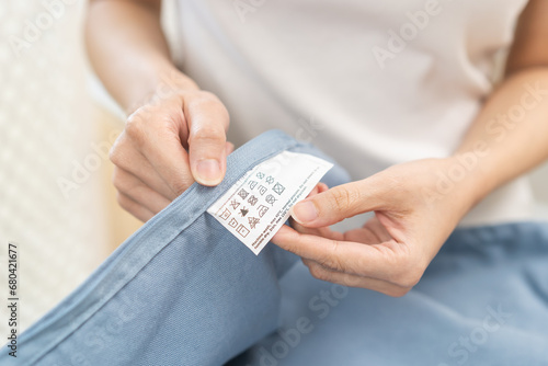 Housewife asian young maid woman hand holding shirt label, tag with instructions, guide before cleaning clothes, fabric into washing, drying machine. Household, chores working at home, laundry concept